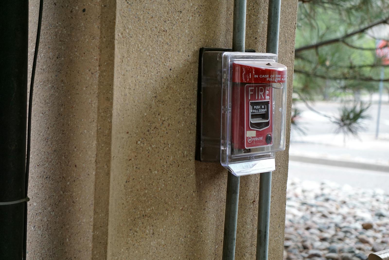 Close-up view of a red fire alarm mounted on a textured outdoor wall, showcasing safety equipment.